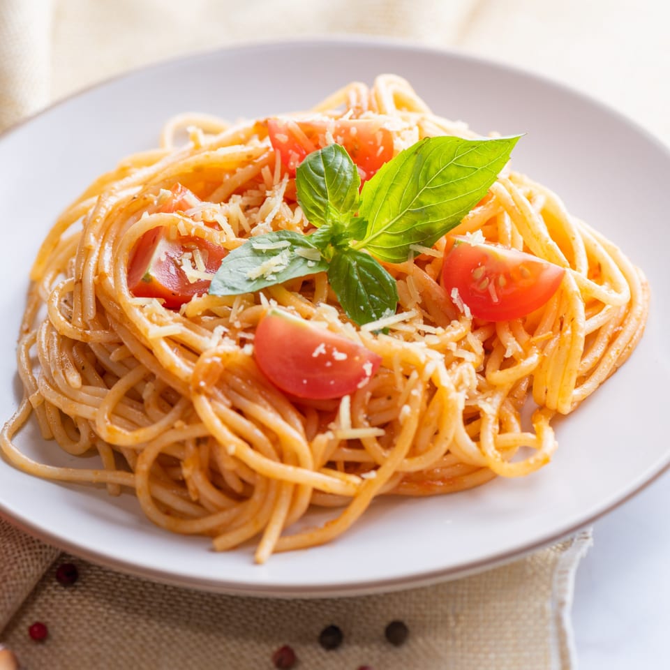 Spaghetti with tomato sauce, cherry tomatoes, grated cheese, and fresh basil on a white plate.