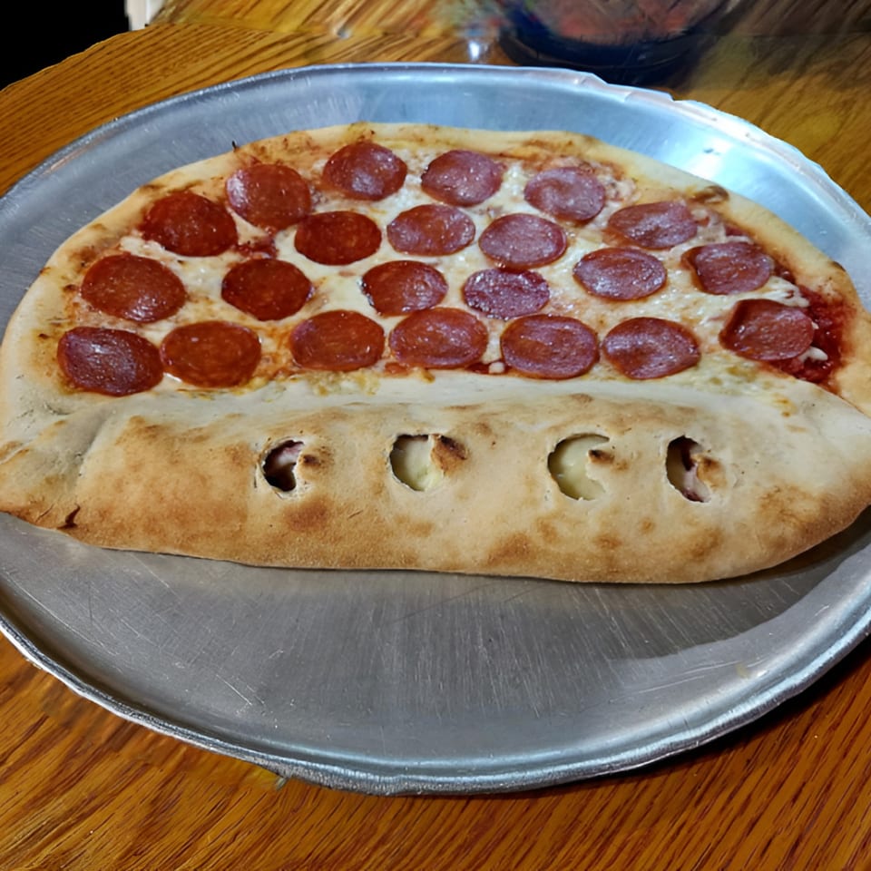 A half-pizza, half-calzone with pepperoni and cheese on a metal tray.