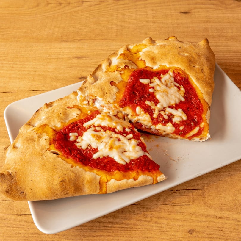 Two halves of a calzone with red sauce and melted cheese on a white plate.