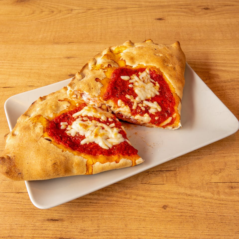 Two halves of a calzone, filled with red sauce and melted cheese, on a white plate.
